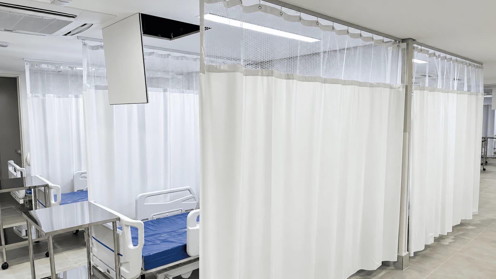 Cortinas divisórias brancas instaladas entre leitos hospitalares, com tela superior e trilhos no teto.